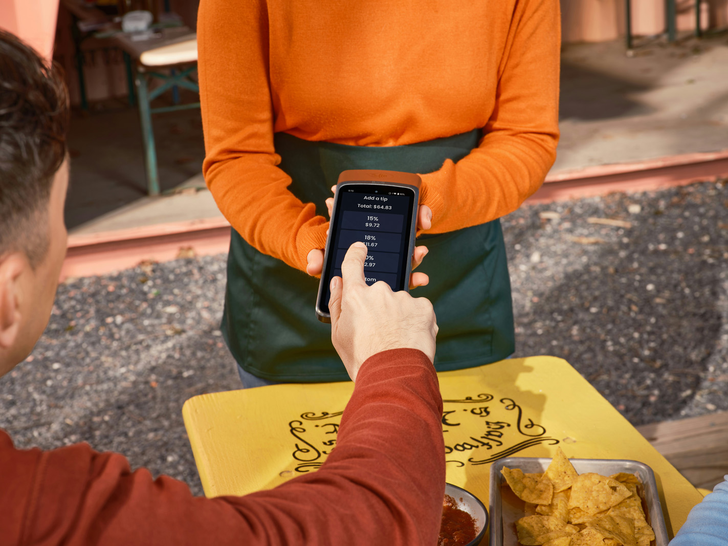 A park guest tapping a cashless wristband to pay at a bright food and game stand