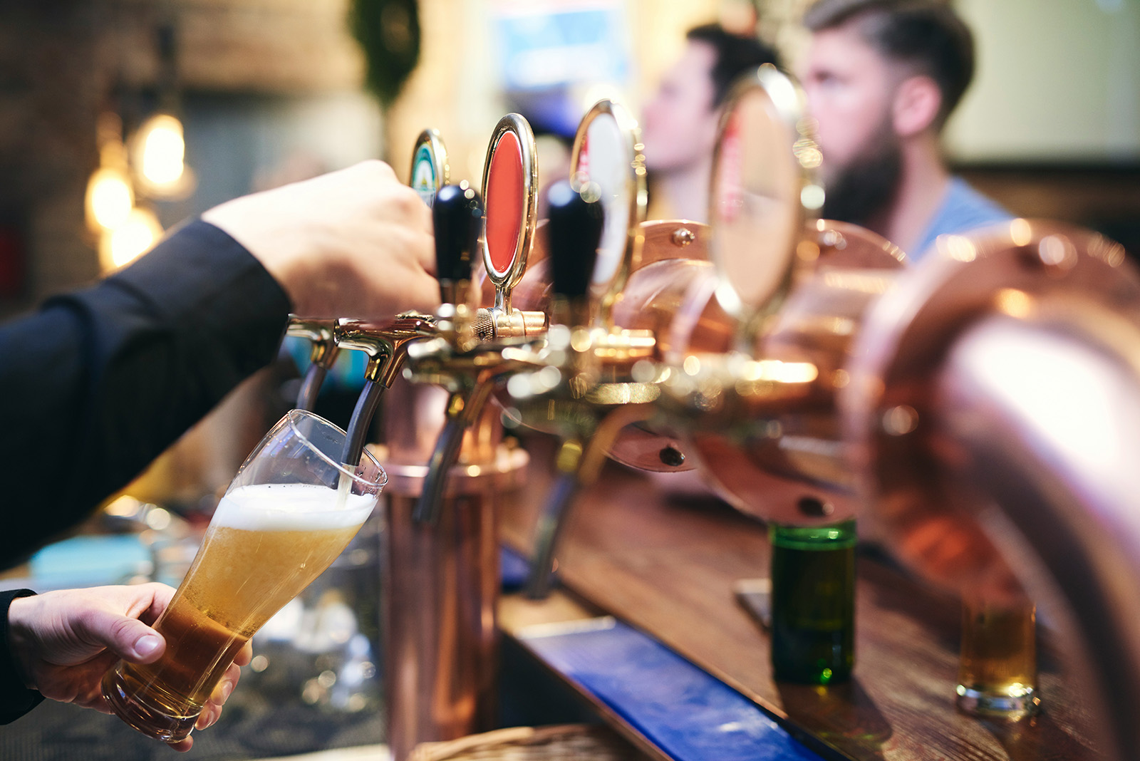 A bartender pulling a pour at a busy brewery taproom; flights on the bar and branded glassware