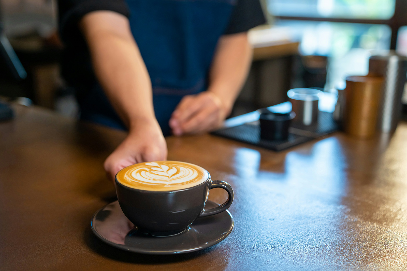 Cozy cafe; a barista passing a coffee to a smiling customer in warm morning light