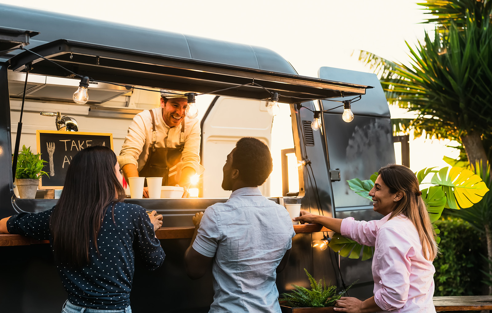 A lively food truck at an event; staff handing food through the window with festival, street-food energy