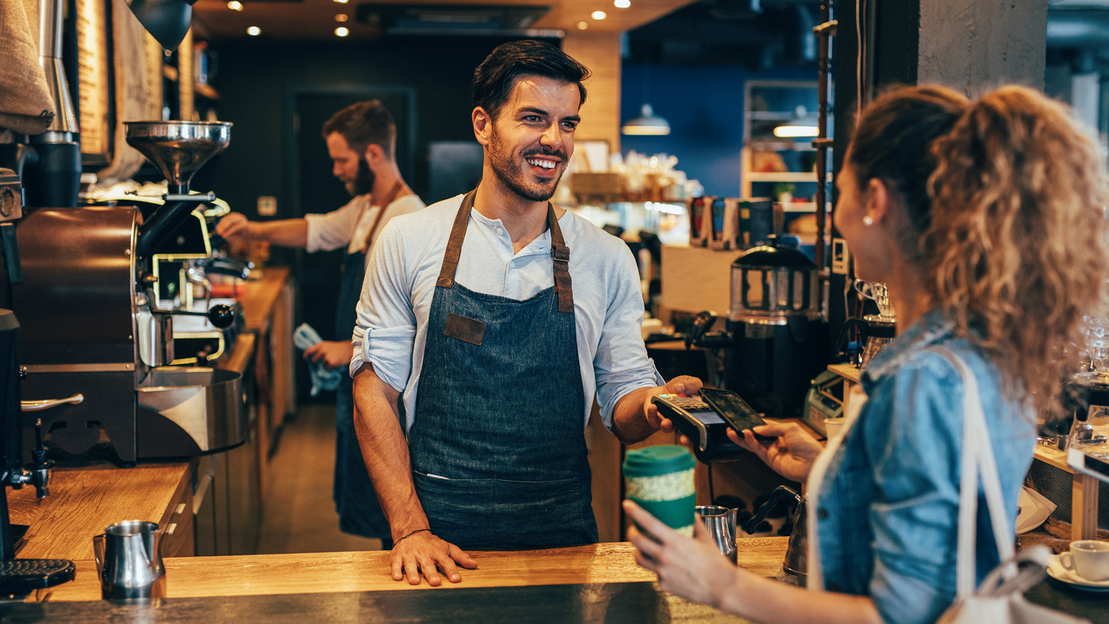 A customer tapping a card or phone on a sleek terminal at a counter; crisp, modern, frictionless