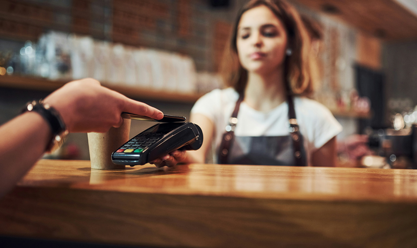 Wireless handheld smart terminal accepting a contactless tap payment, with a countertop and mobile device lineup