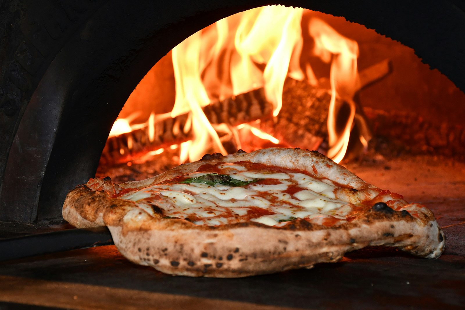 Pizzaiolo working the counter beside the oven in a busy pizzeria